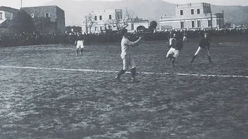 Un partido en el campo de la Carretera de Horta, con las casas del barrio tras la línea de banda